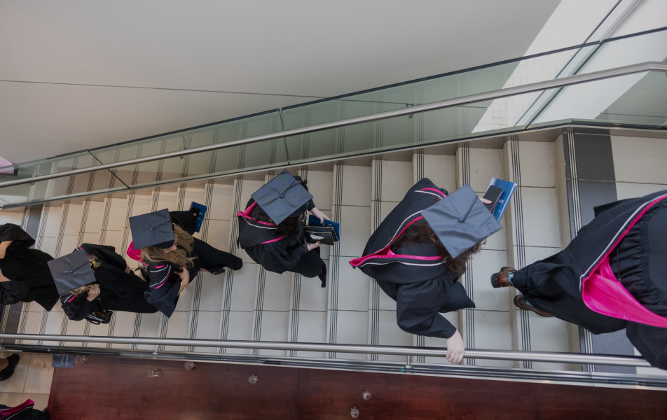 Graduates in cap and gown walking up a flight of stairs