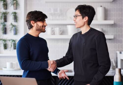 two gentlemen wearing sweaters shaking hands, man on left has a beard.